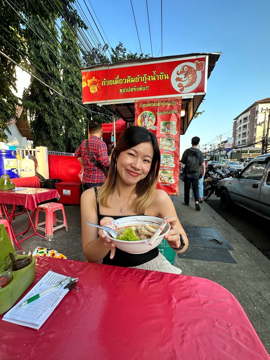 Cherry sonriendo frente a un plato de sopa de fideos en un puesto callejero de Tailandia