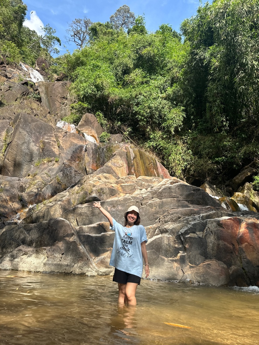 Cherry dentro del río frente a una cascada entre rocas y selva